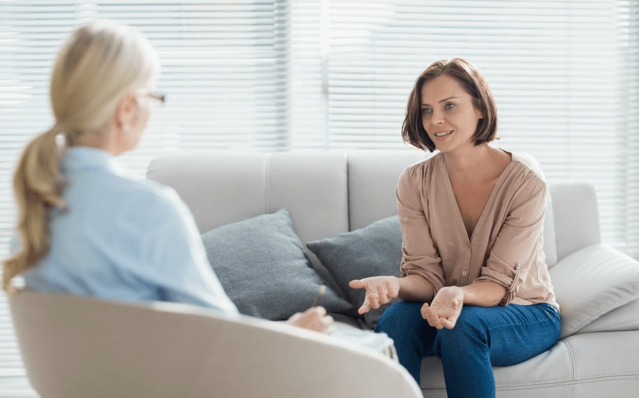 Two women engage in a conversation on a sofa in a bright, modern room.
