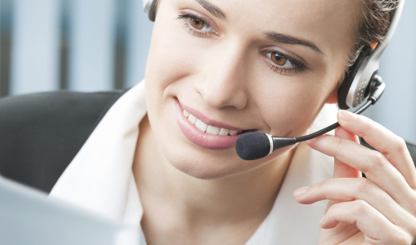 Smiling woman wearing a headset, engaged in a conversation while holding a paper.